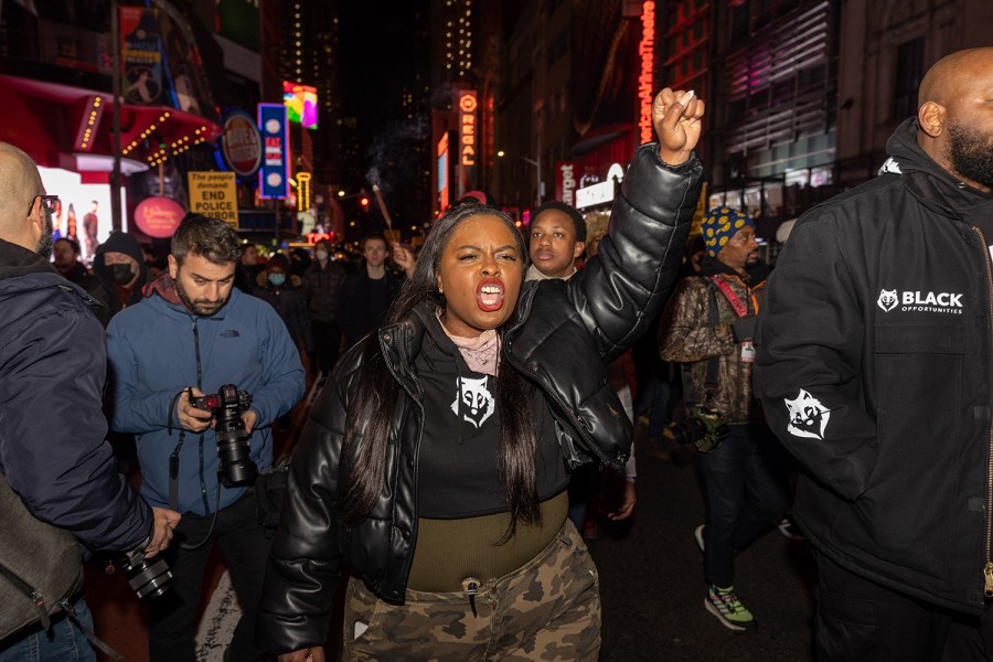 A woman stands in the middle of a crowd of protesters in Times Square. She shouts and raises her fist.