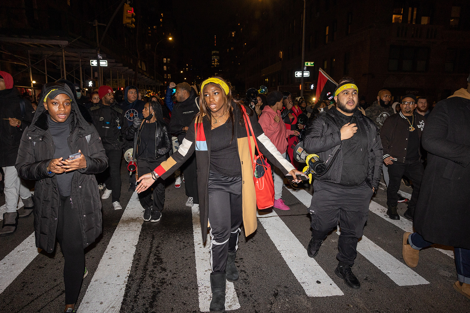 Three protesters wearing yellow bandanas stand in a line among other protesters in Times Square.