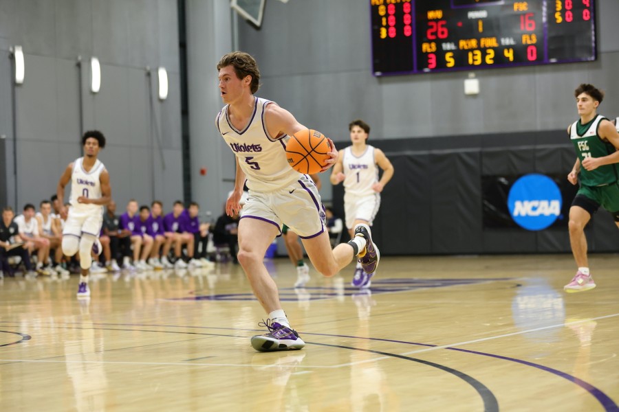 Five male basketball players running on a basketball court. In the center is a player wearing a white and purple N.Y.U. jersey with the number five. He is running with the ball in his left hand.