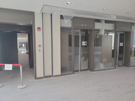 An elevator entrance, blocked off by a red line. The glass covering the elevator shaft is dusty.