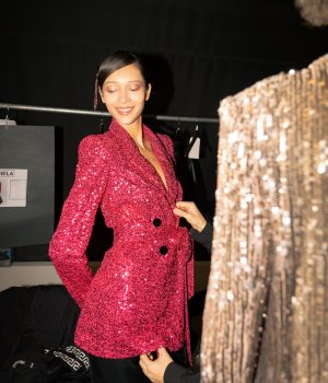A flash photograph of a model with slicked back black hair getting fitted in a sparkly red blazer.
