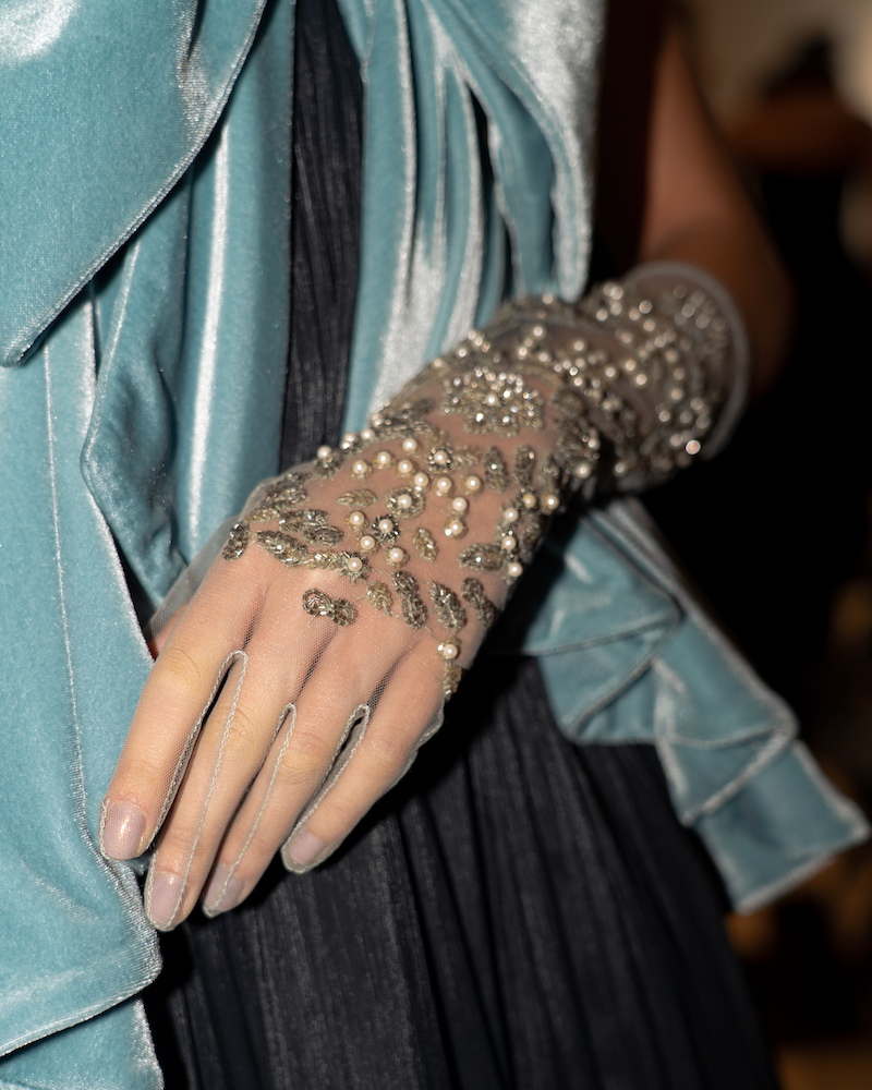 A flash photograph of the detailing of light blue, lace, sparkly beaded gloves.