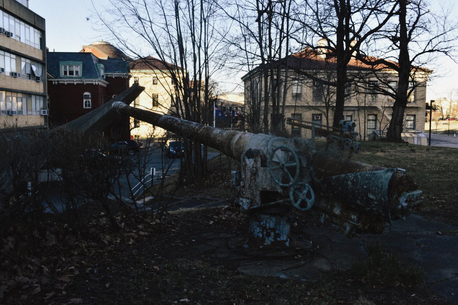 A rusted cannon gun in front of several buildings.