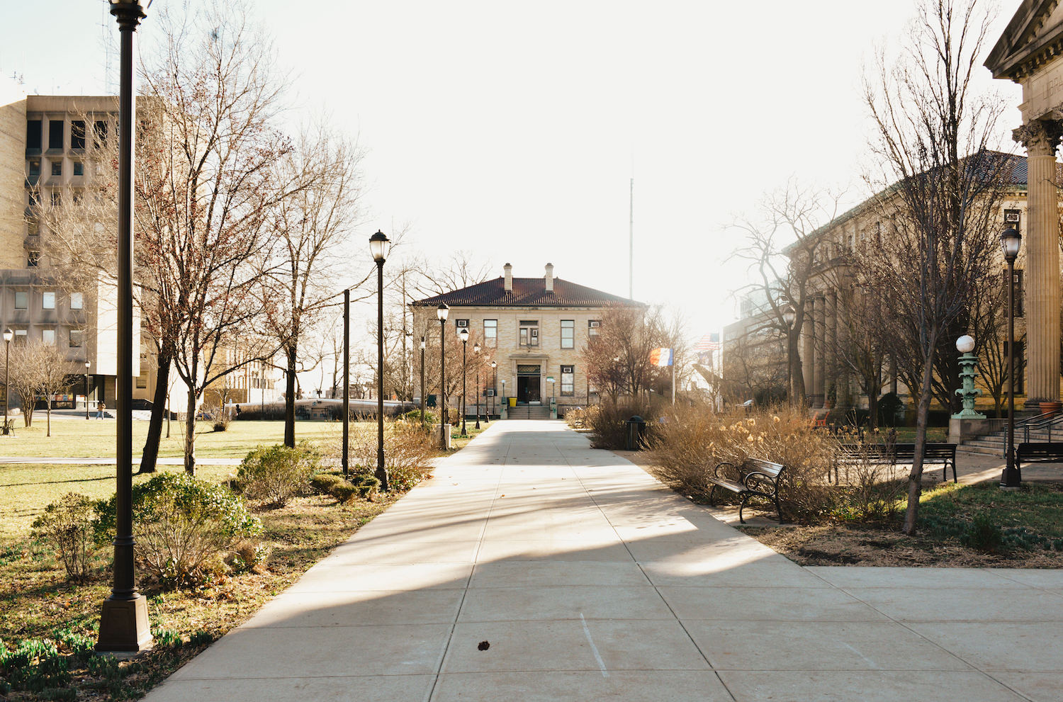 A two-story house sit in the middle of the frame. In front of the house is a marble walkway with street lamps and trees on the side.