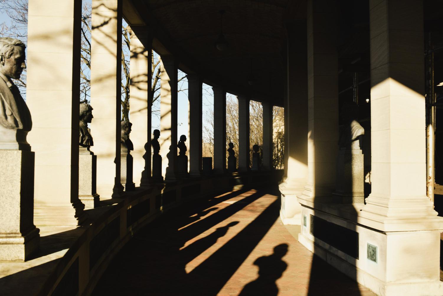 Statues in the Hall of Fame of Great Americans. There are shadows on the ground of the columns and the statues.