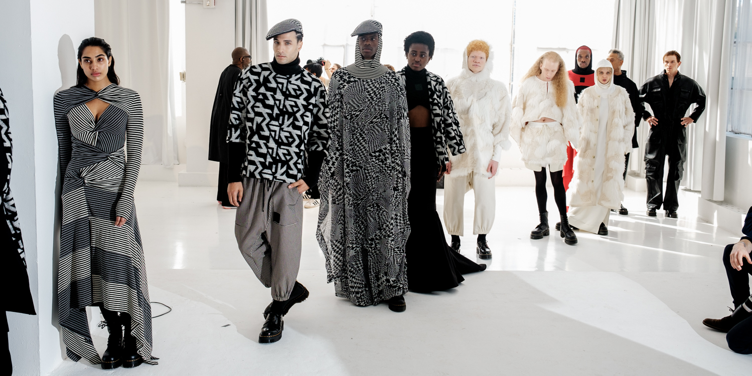 A group of models stand in a diagonal line. Most wear black-and-white outfits, with one model in the back wearing black and red.