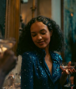 A model wearing a blue sequined dress holds a martini glass.