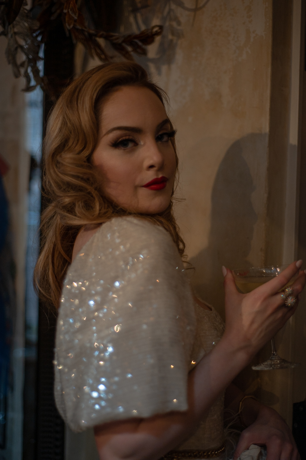 Elizabeth Gillies wearing a white sequined dress and holding a martini glass.