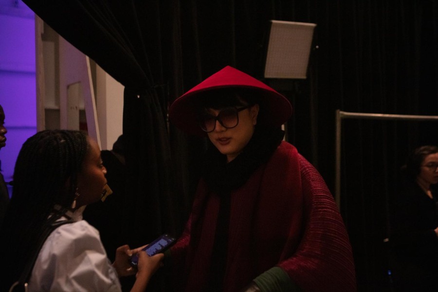 Chocheng brand designer Cho Cho Cheng being interviewed. He wears red outerwear and a red conical hat.
