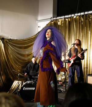 Model dressed in a purple tulle hat, brown coat with purple ruffles, and patchwork jeans designed by Paradoxvestedrelics, Yxen, and Kids Destroy.