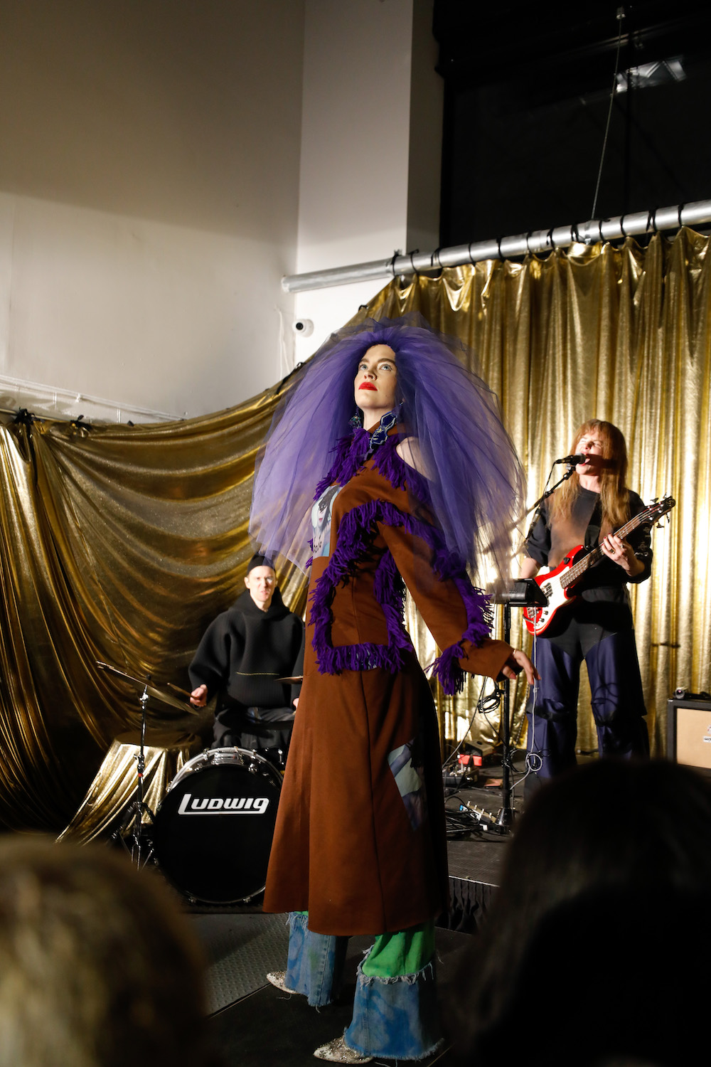 Model dressed in a purple tulle hat, brown coat with purple ruffles, and patchwork jeans designed by Paradoxvestedrelics, Yxen, and Kids Destroy.