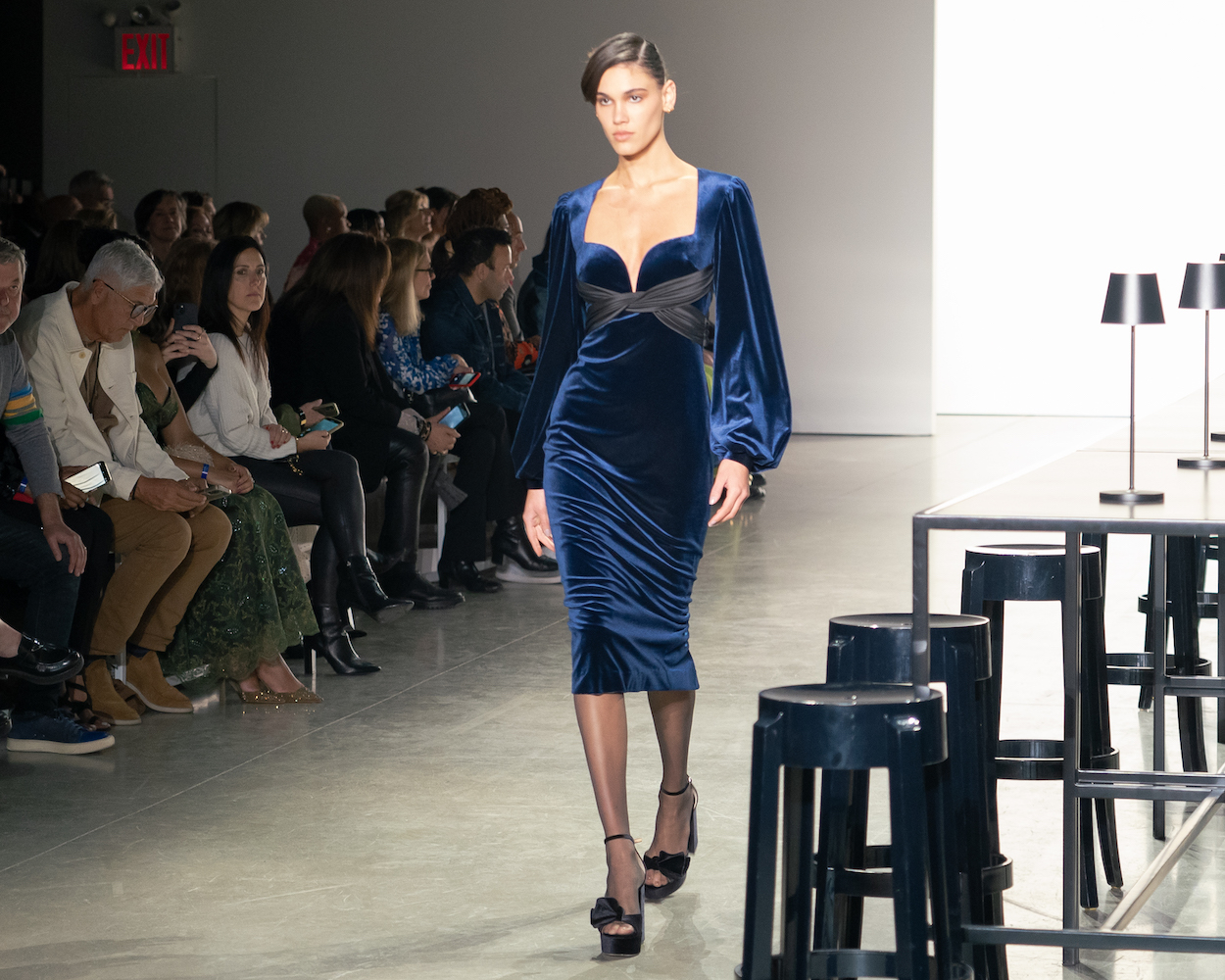 A model walking down the runway in a velvet blue dress with balloon sleeves and black heels.