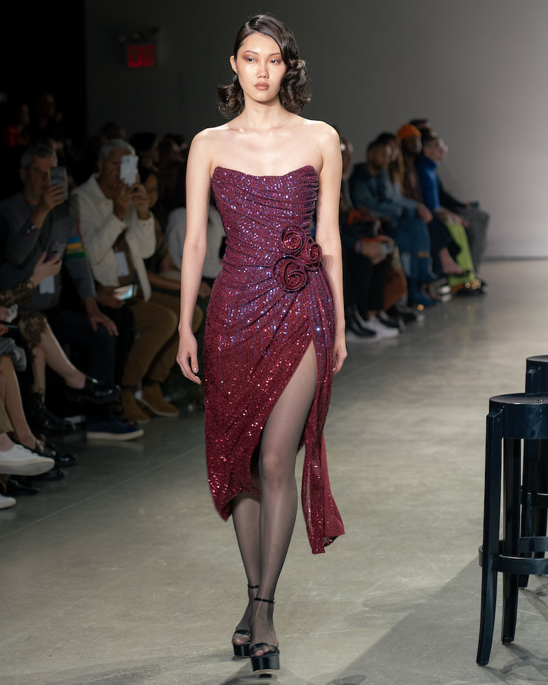 A model walking down the runway wearing a sparkly maroon dress and black heels.