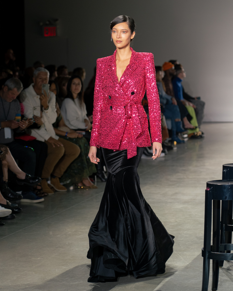 A model walking down the runway wearing a sparkly red blazer and a long, black mermaid skirt.
