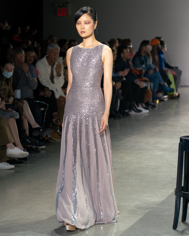 A model walking down the runway wearing a sparkly, pastel purple dress and silver heels.
