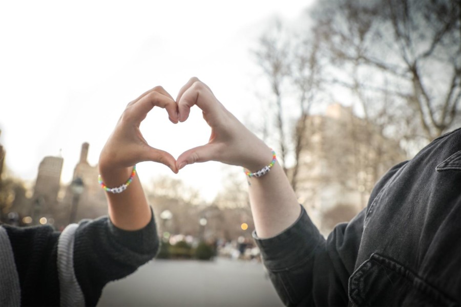 Two people making a heart with their hands together in Washington Square Park. They are wearing matching friendship bracelets.