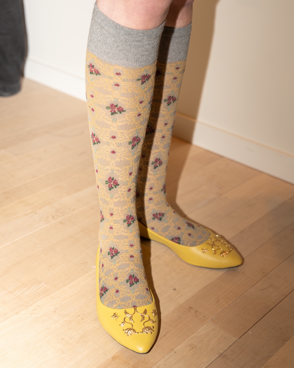 A photograph of embellished yellow flats with high-rise socks that feature a yellow, gray and red Victorian floral pattern.