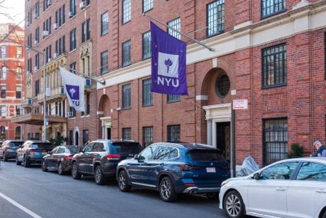 The exterior of NYU’s Lipton Hall with two NYU flags. The building is covered with red bricks and there are several cars parked outside the entrance.