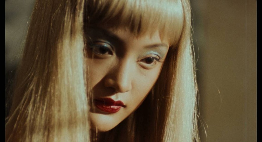Chinese actress Zhou Xun, who plays the dual role of Moudan and Meimei in the film Suzhou River. She has long, blonde hair with bangs, blue eyeshadow and red lipstick.