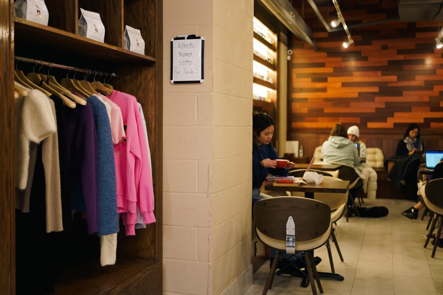 The interior of a coffee shop with customers sitting on the right side and a rack of clothing on display on the left side.
