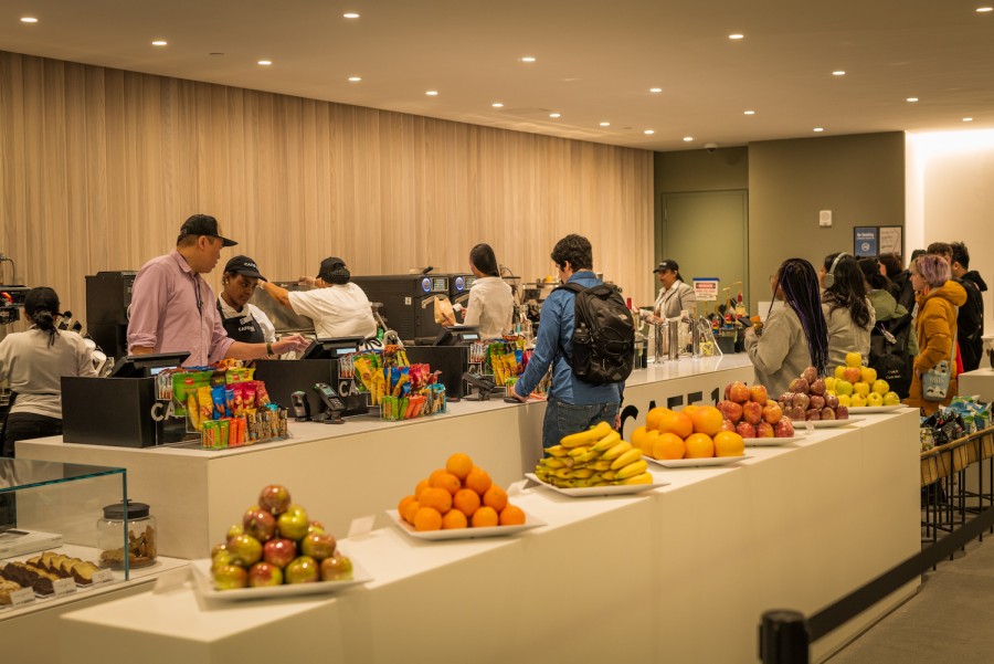 In+the+warmly-lit+dining+hall+in+the+Paulson+Center%2C+a+line+of+students+wait+next+to+the+cashier+counter.+Seven+plates+of+neatly-arranged+fruits+are+placed+on+a+white+table.