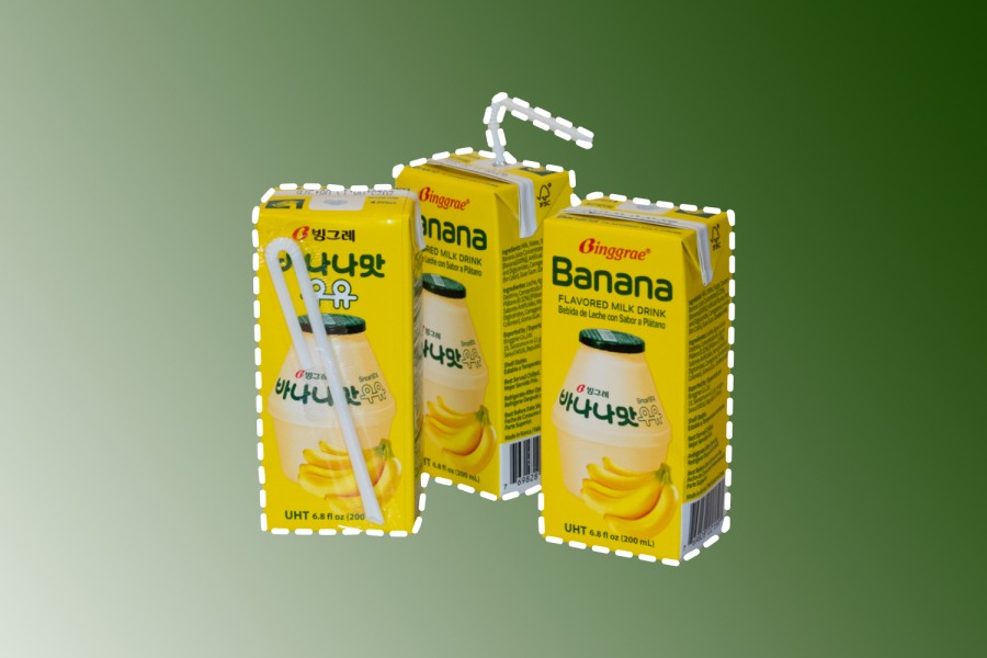 Three boxes of banana milk against a green gradient background. The boxes are yellow and have the word “banana” written on top with images of bananas and banana milk underneath.