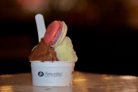 A small cup of ice cream on a table. There is a macaron on top of the ice cream. The cup is labeled “Amorino Gelato Al Naturale.”