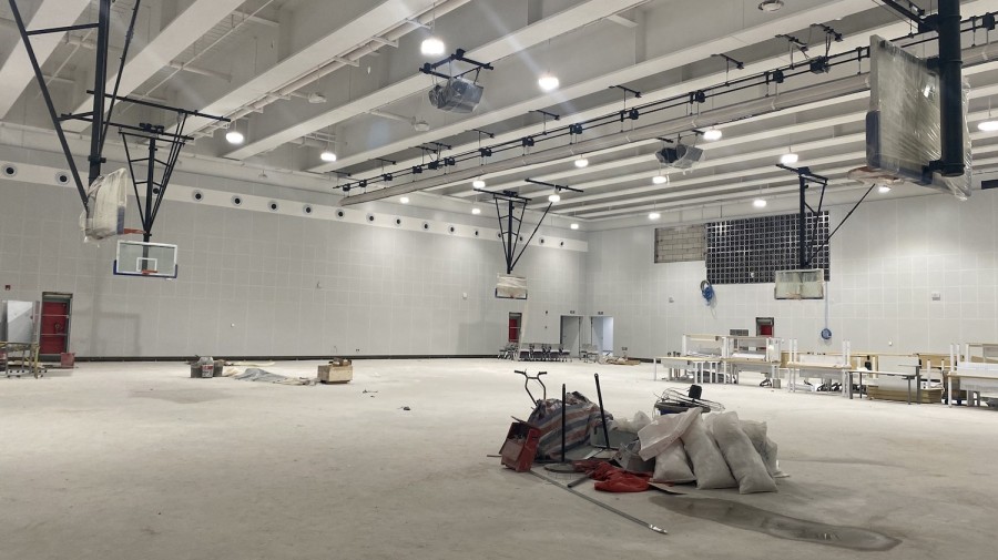 The interior of an indoor basketball court under construction. Construction equipment and furniture are scattered across the floor.