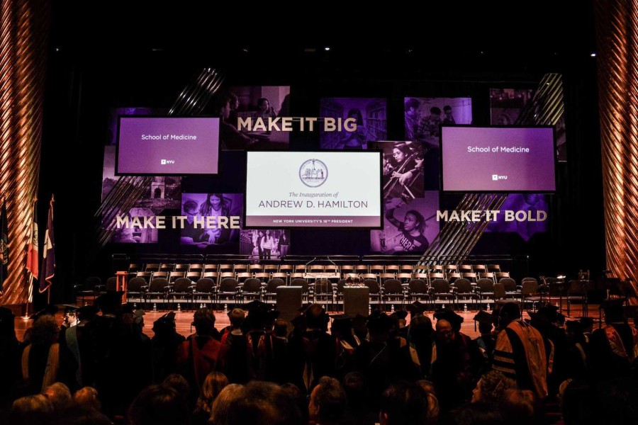 The interior of the Skirball Center. A crowd of ceremony attendees gather in front of a projected screen that reads Make It Big, Andrew D. Hamilton, Make It Here, Make It Bold.