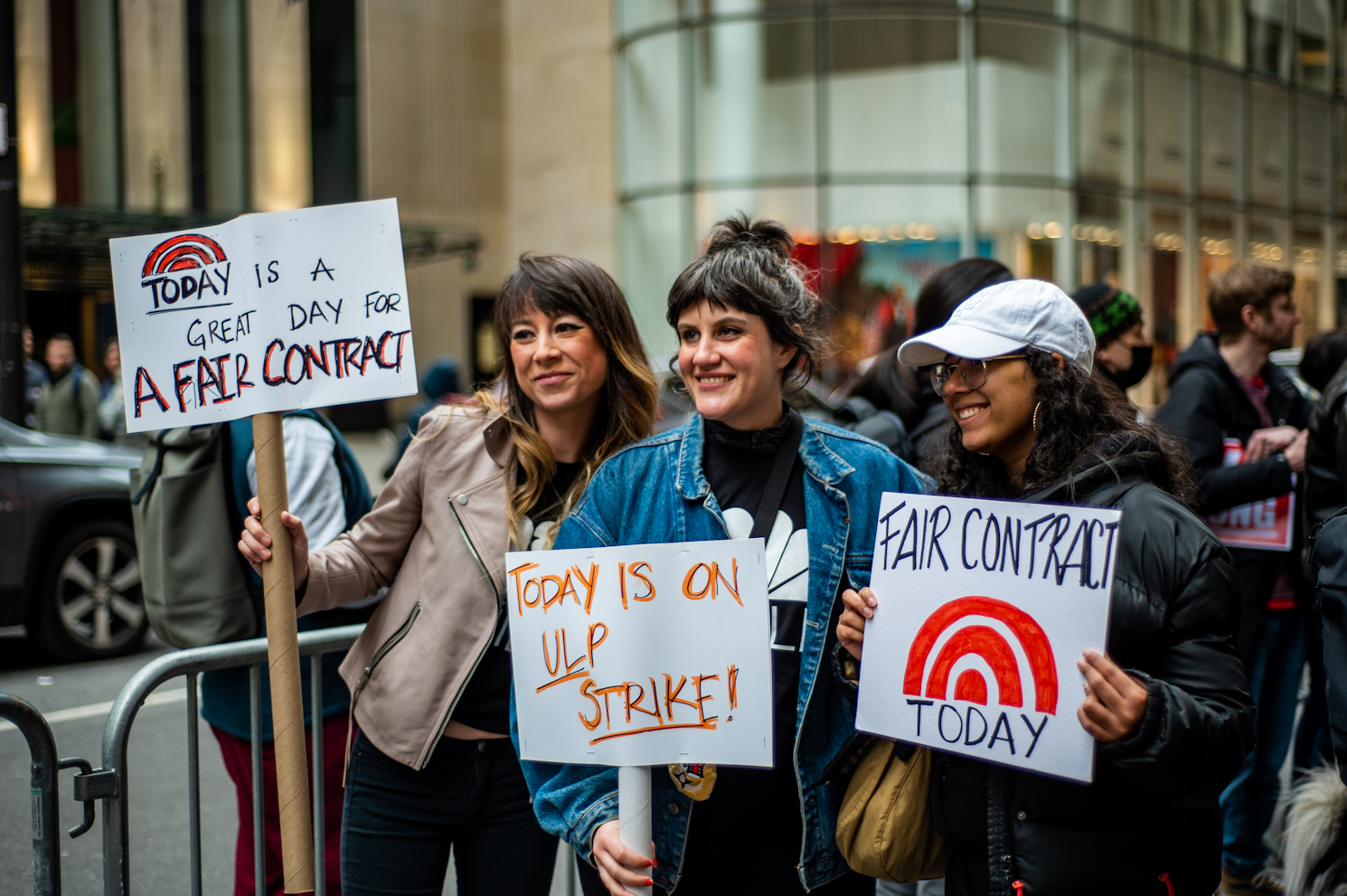 Three women pose with signs advocating for a fair contract.