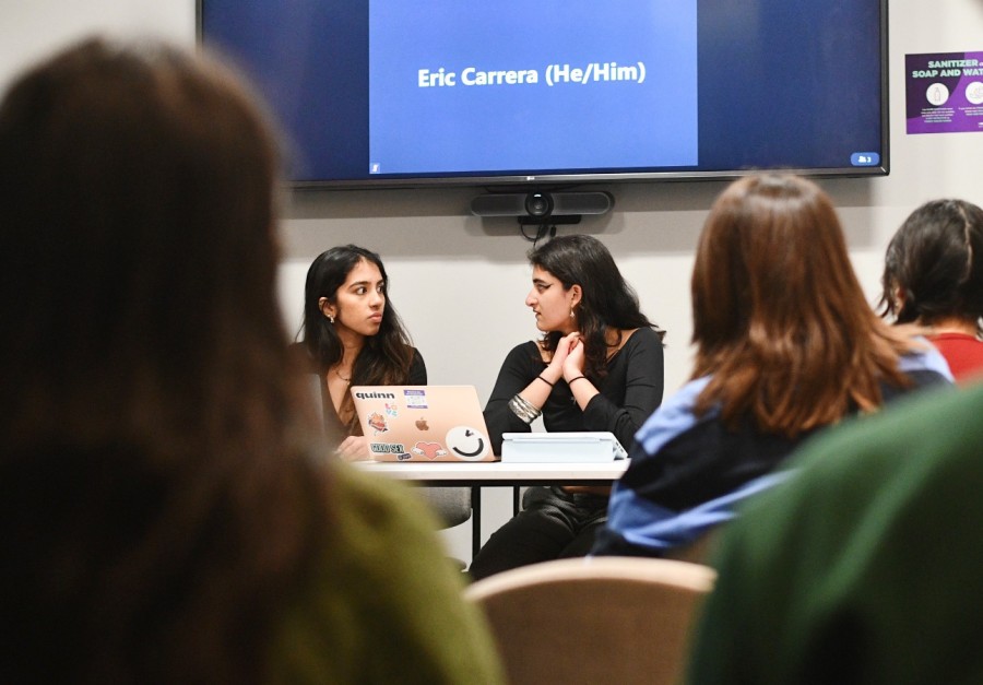 Two speakers sit behind a white table and in front of a television, holding a forum about abortion inside a university classroom. In front of them is a group of people.