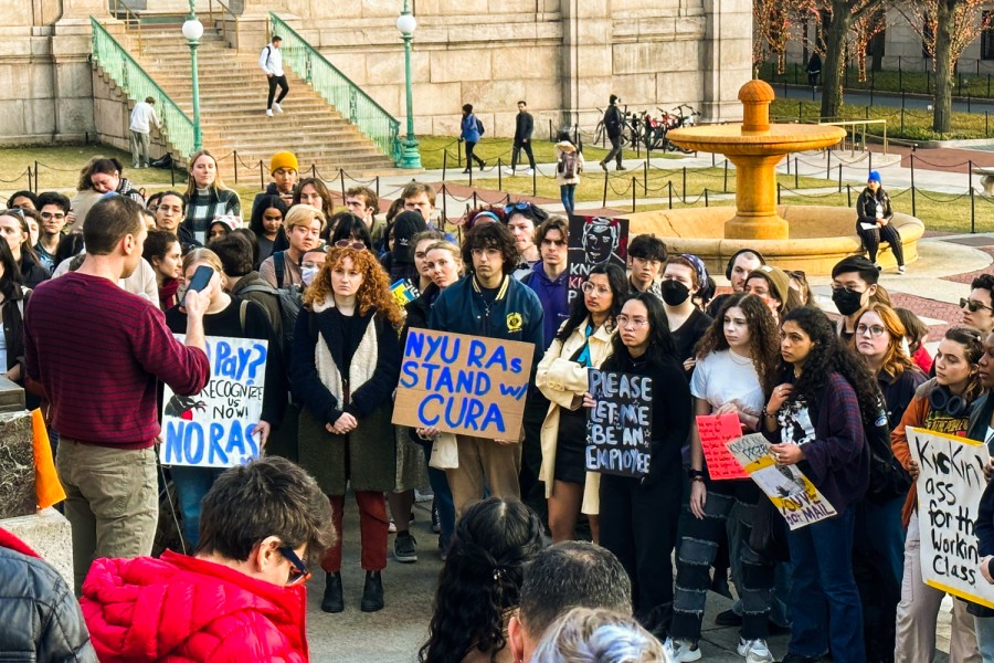 A group of rally attendees stand in front of Columbia University’s Alma Mater statue. A cardboard sign with blue text reads “N.Y.U. R.A.s. Stand With C.U.R.A.”