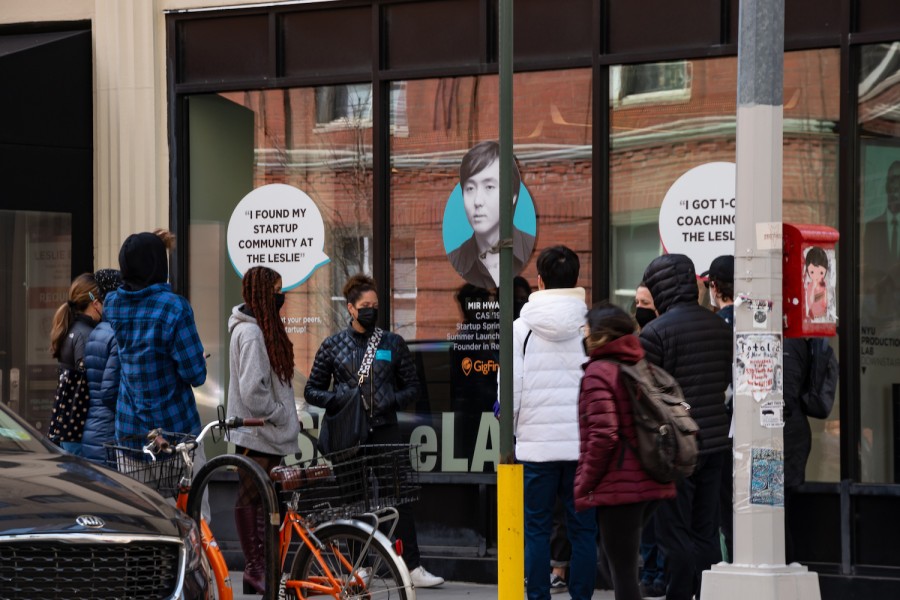 A group of visitors stands outside a university building that has glass windows with posters on them.