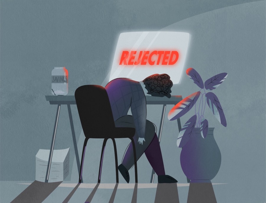 An illustration of a person sitting in front of a desk with their head resting on the table. They are looking at a screen with the word “rejected” written in red. On the left side of the desk is an empty jar labeled “savings.” There is a large stack of papers under the desk with a large potted plant to the right.