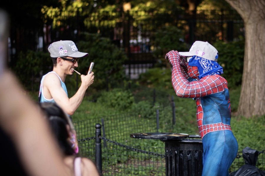 A visitor to Washington Square Park uses a phone to take a picture of a performer dressed in a blue and red Spiderman costume.