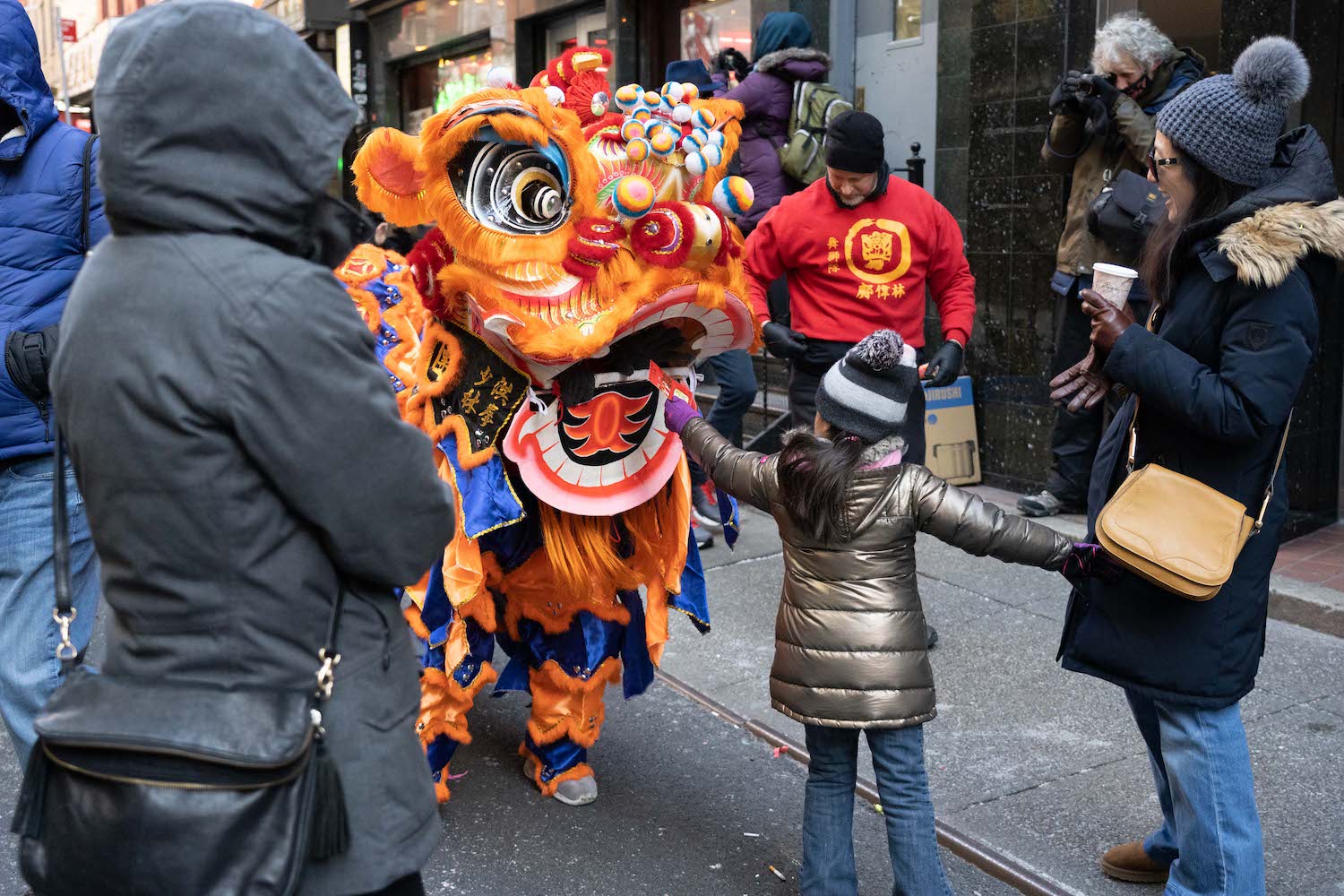 A child handing a red packet into a lion dancer’s costume’s mouth.