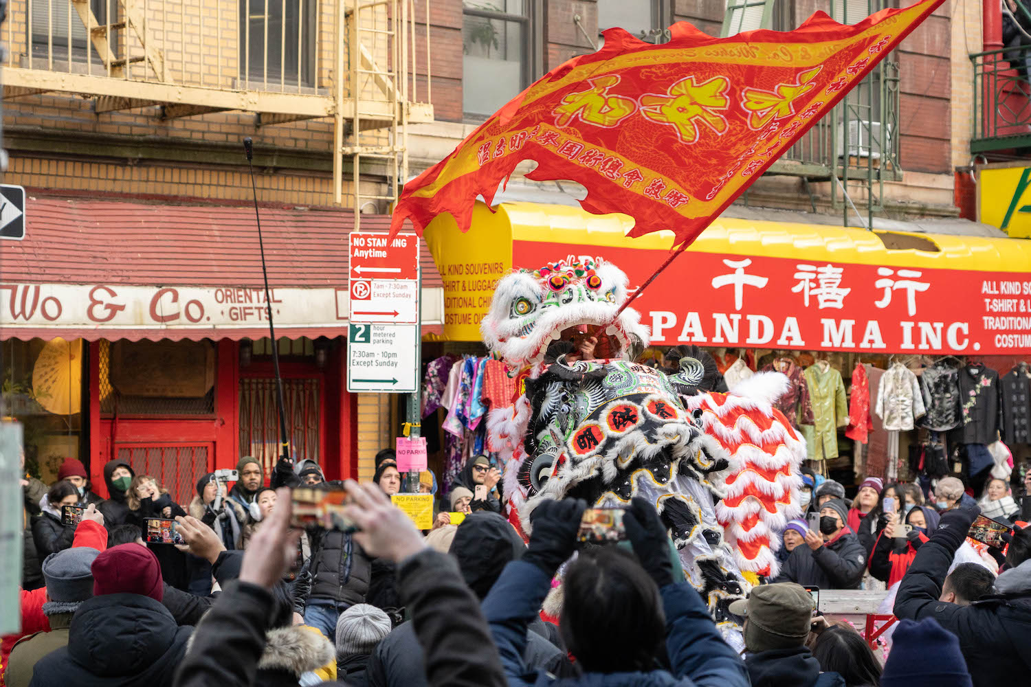 A lion dancer waving a red flag on a stage in front of a store.