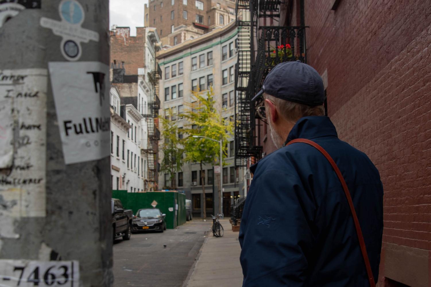 Alan Grossman, wearing a blue jacket and a blue cap, walks down a narrow street.