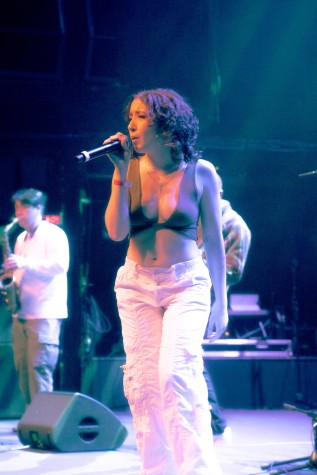 Sophia Abraham wearing a black crop top and white cargo pants sings on stage.