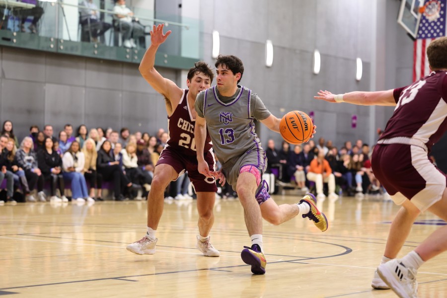 Wearing a gray jersey with a purple number 13 printed on the top, a basketball player is dribbling a basketball with his left hand. Raising his right hand, his opponent, who is wearing a ruby jersey, is defending from behind.