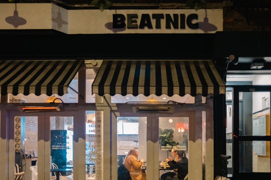 The storefront of a restaurant with the word “Beatnic” written above the windows. There are three people dining inside the restaurant.