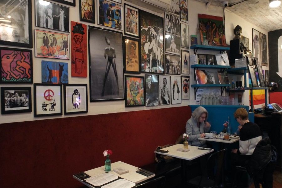 Two customers share a meal in the colorful interior of Urban Vegan Kitchen. Many framed pieces of art hang on the wall behind them.