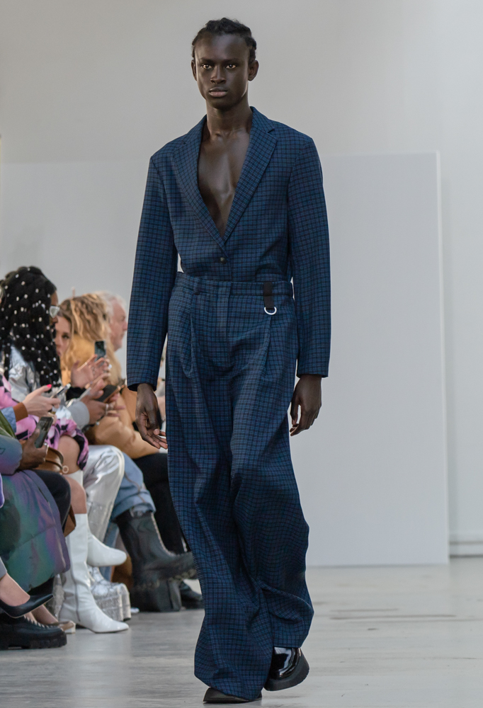 A model walking down the runway wearing a checkered blue v-neck suit.