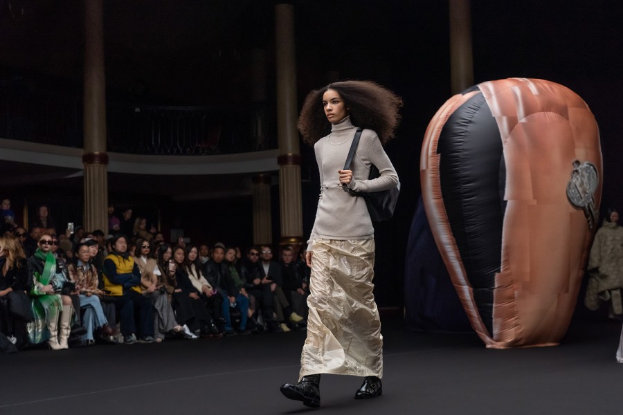 A model in a gray turtleneck and a white skirt who is holding a black shoulder bag at the 2023 E.E.N.K. Paris Fashion Week show.