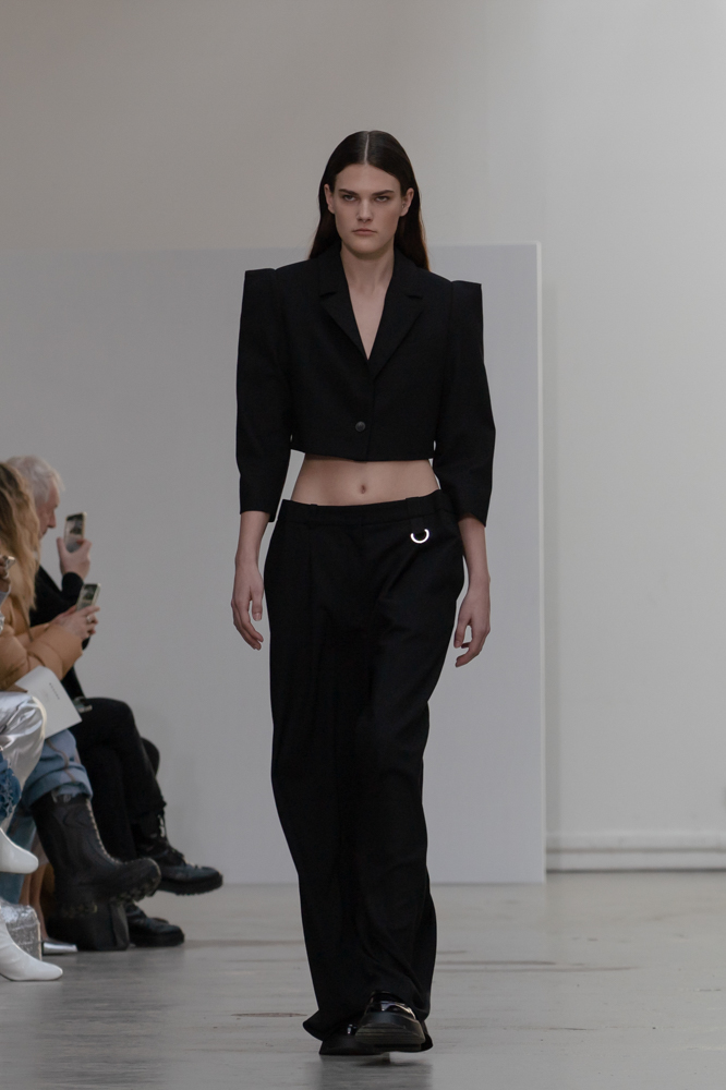 A model walking in a cropped black shoulder-padded blazer and loose-fitted trousers.