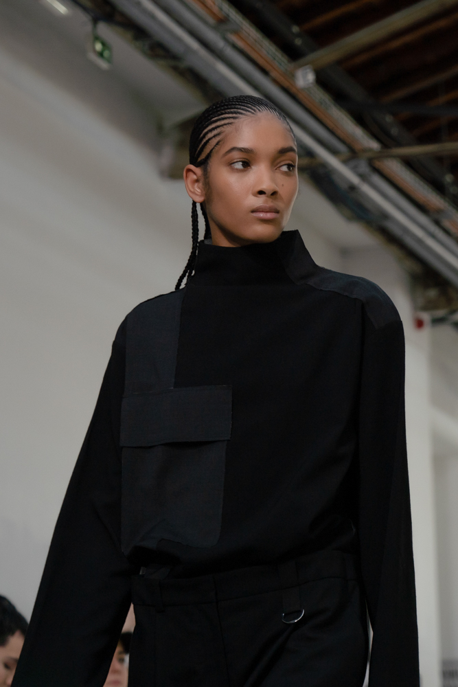 Close-up of a model walking down the runway in a black and gray patched shirt.