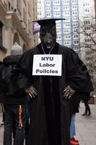 An attendee dressed as a rat poses for photo, carrying a sign that reads "N.Y.U. Labor Policies."
