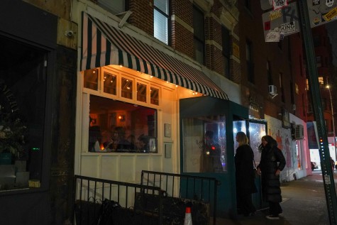 The exterior of a restaurant at night. The storefront is fixed with a black-and-white striped awning.