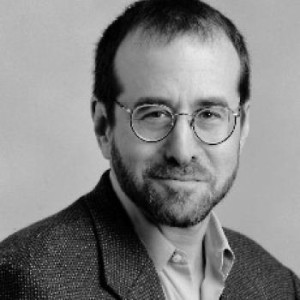 A black-and-white headshot of NYU professor Mark Crispin Miller wearing a suit.