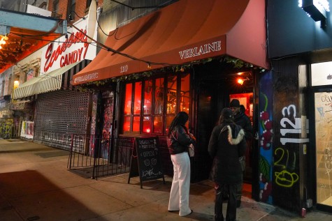 The exterior of a restaurant at night. The storefront is fixed with a red awning with text that reads, “at.Verlaine.N.Y.C. 110 Verlaine.”